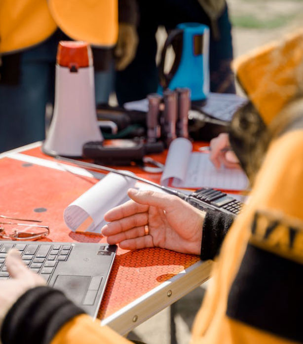 Close up view of someone sitting at a laptop on a table full of various engineering and construction equipment.